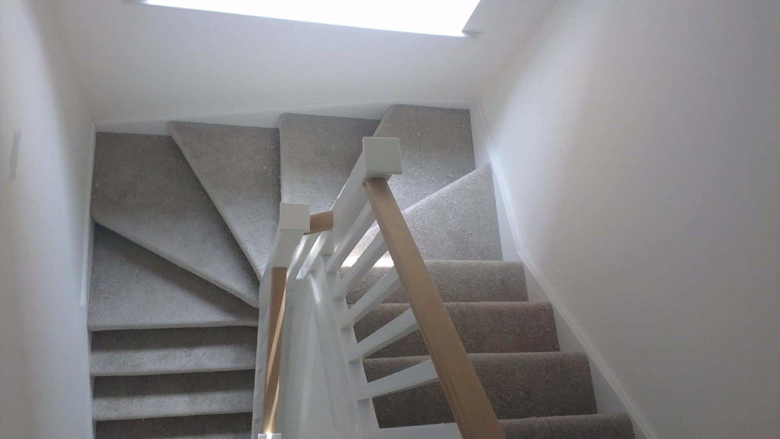 Grey carpet fitted up a winding staircase with a white and oak banister