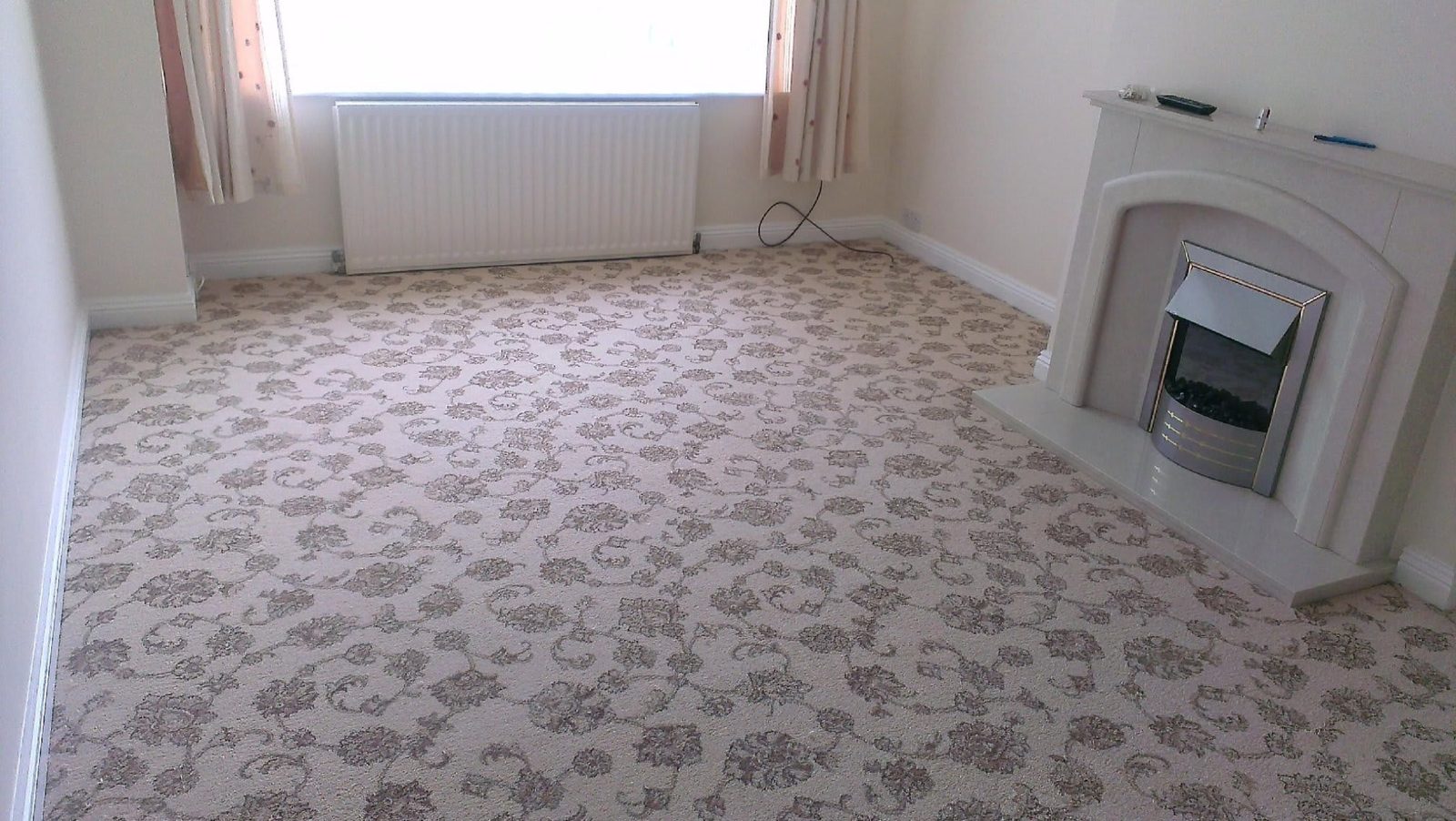 Patterned beige carpet fitted in a living room with a fireplace