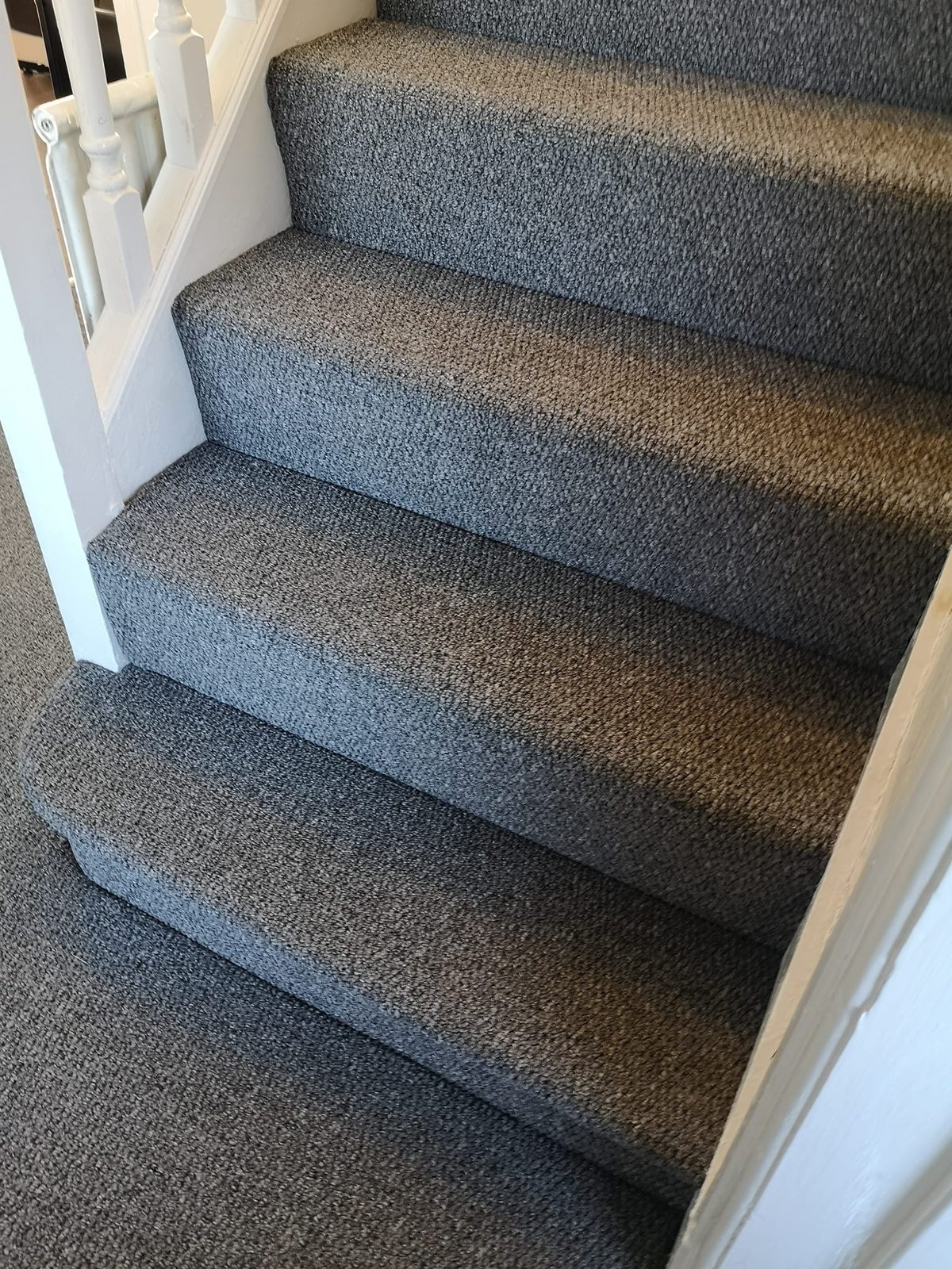 Grey carpet fitted on a flight of stairs with white spindles